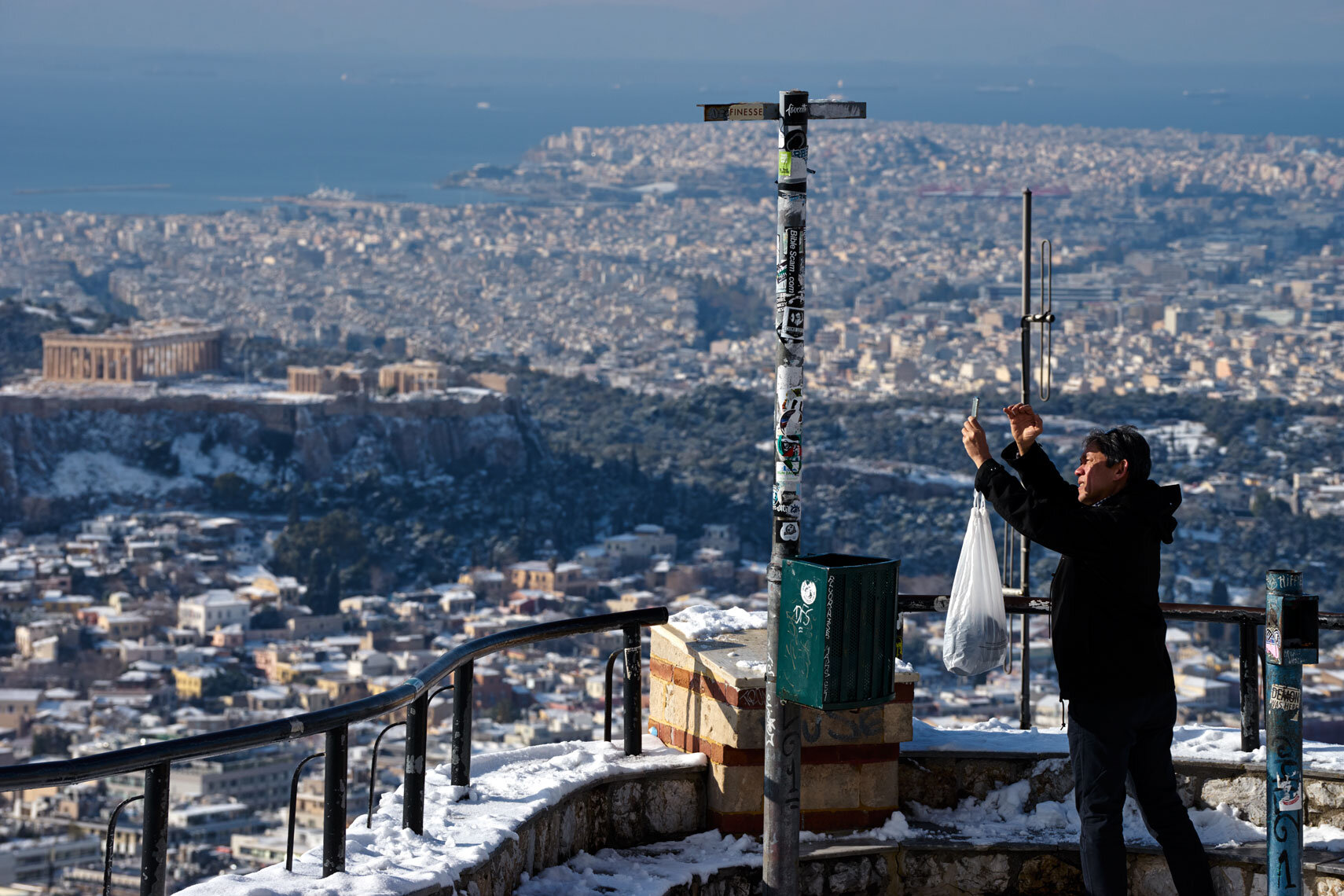 A tourist photographs athens in the snow from Lycabettus Hill.